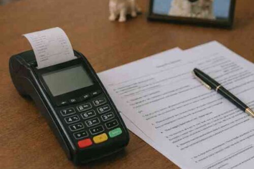 Terminal de paiement avec un reçu en cours d’impression, accompagné de documents administratifs et d'une photo d'un chien sur le bureau.